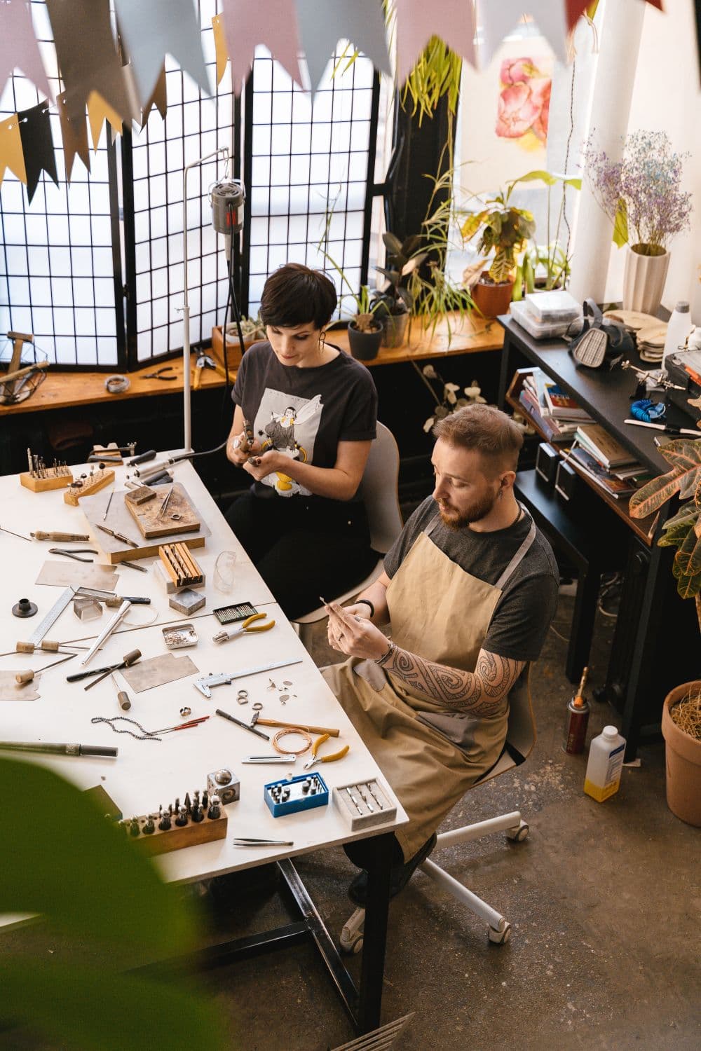 Two artisans making jewelry at a shared workshop bench